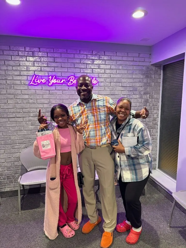 Dr. Kishawn Kole-James with two patients in front of the Live Your Best Smile neon sign