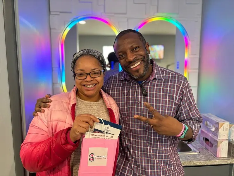 Two smiling Superior Orthodontics patients in front of the rainbow mirror with a pink gift bag